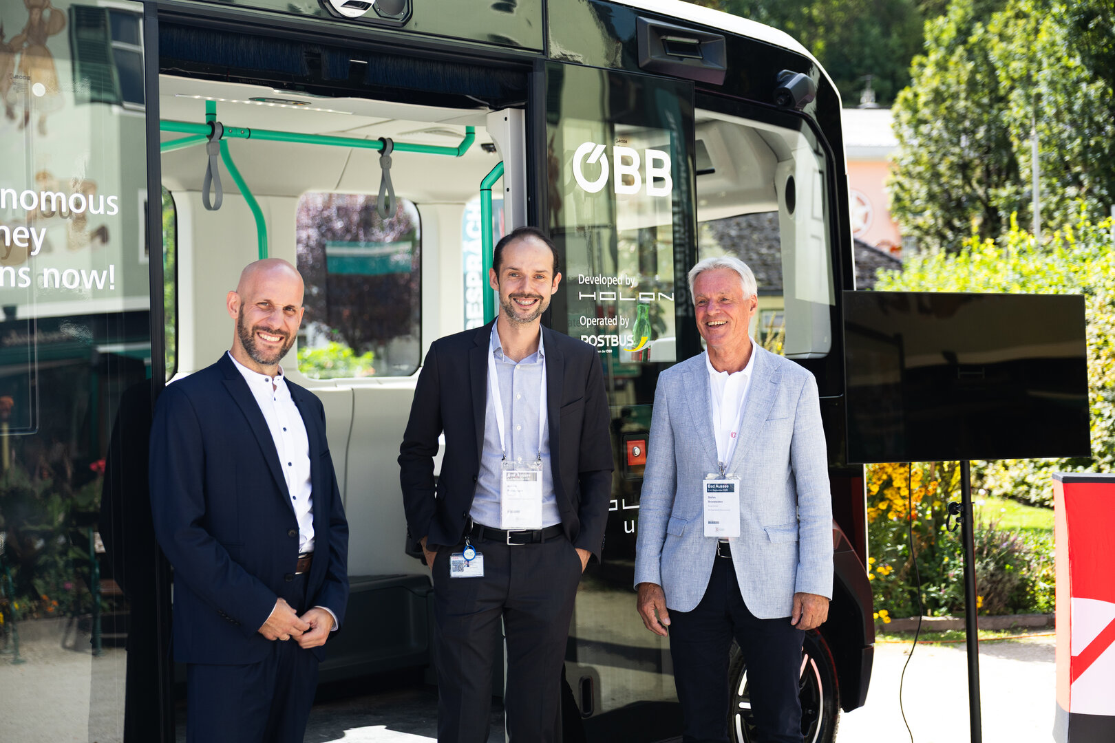 Drei Männer vor einem ÖBB-Bus, links ein Mann mit dunklem Anzug, Mitte ein Mann mit dunklem Sakko, rechts ein Mann mit hellem Sakko.
