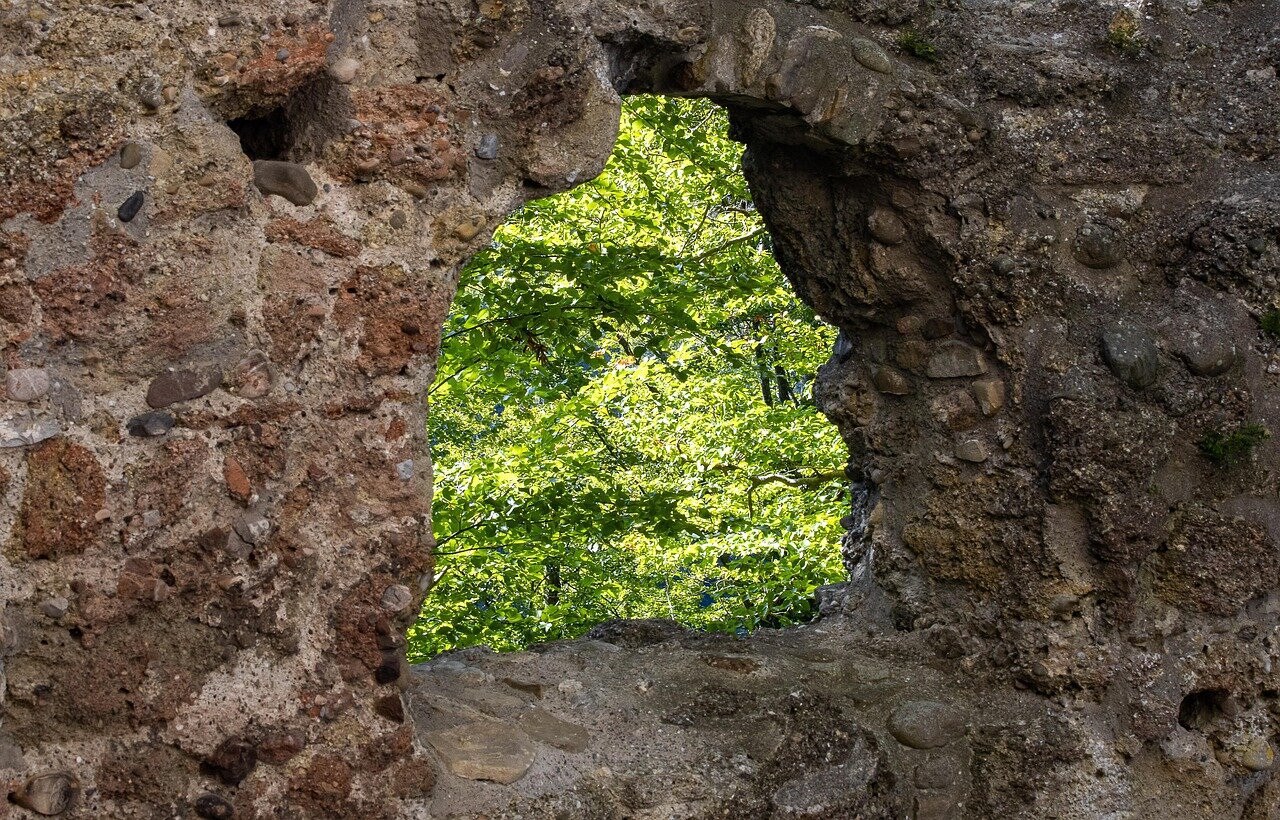 Fenster in Mauer aus groben Steinen mit Blick auf grüne Bäume
