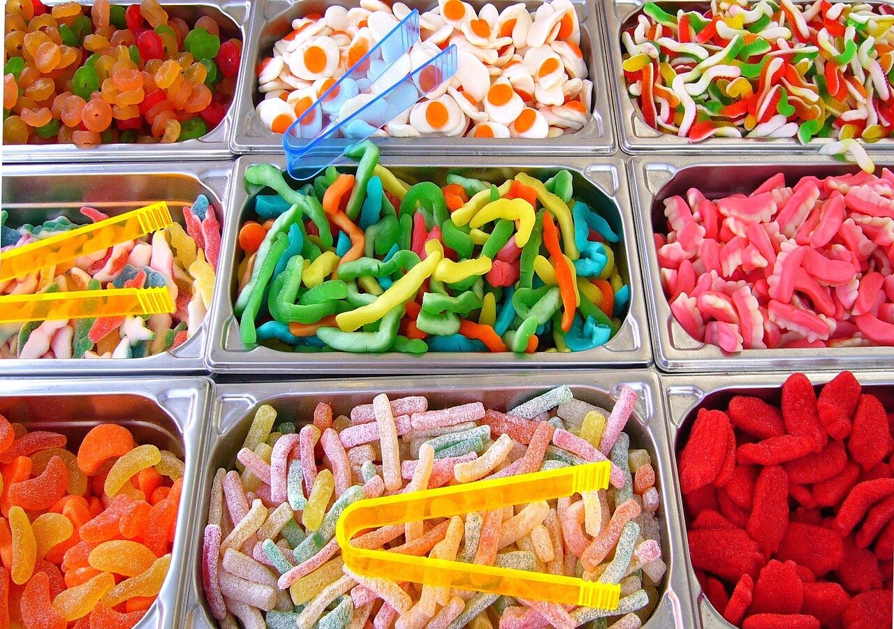 Süßigkeiten in verschiedenen Behältern mit Zangen, bunte Gummibärchen, Fruchtgummi und saure Stäbchen