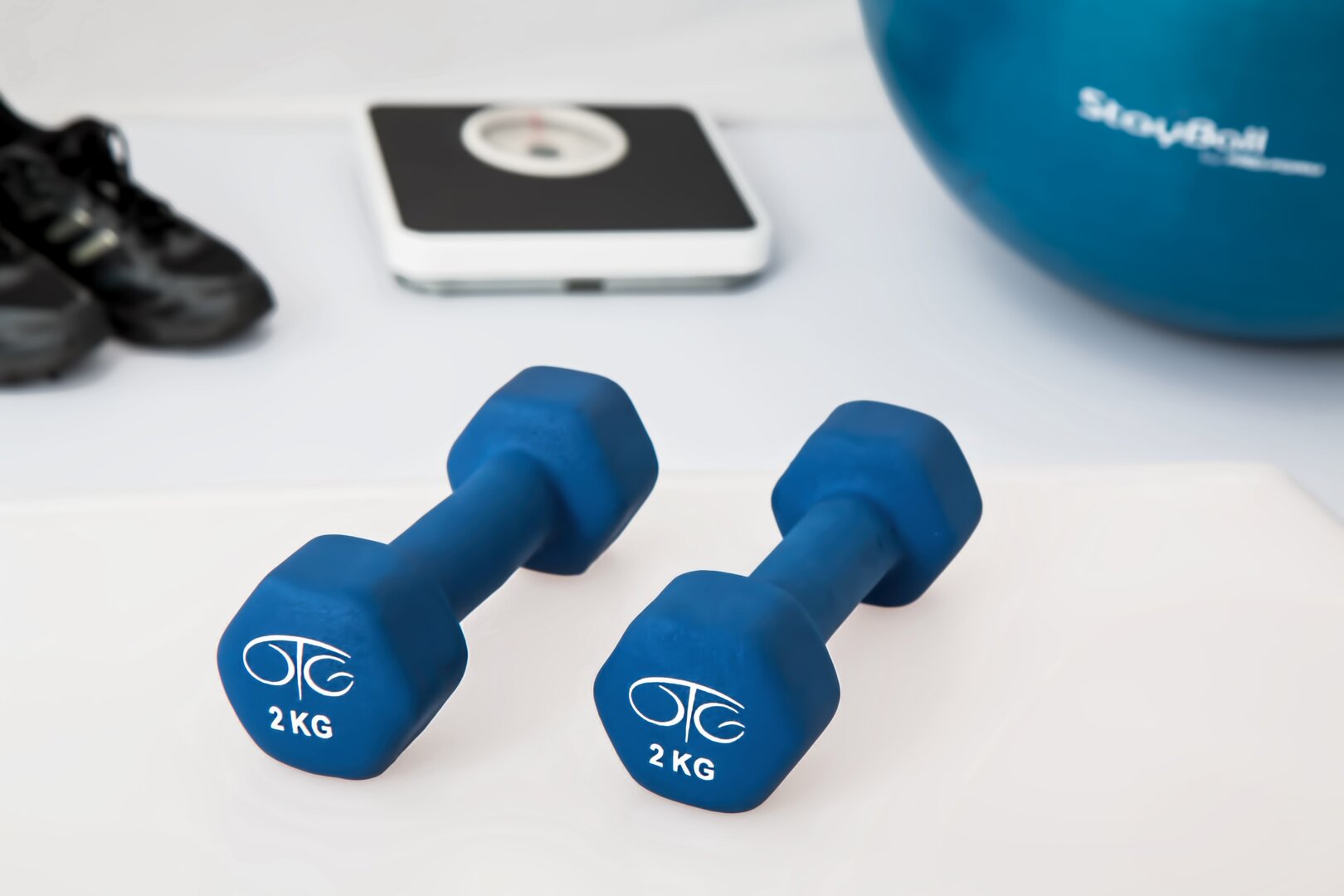 Hanteln 2 KG blau mit Waage und Ball im Hintergrund